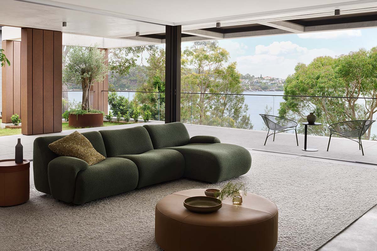 The 1977 Sofa in deep green Leura Mangrove fabric, positioned by the window of a waterfront living room.