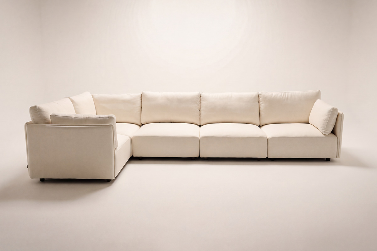 Front-on photograph of an L-shape modular sofa in a beige fabric styled in a studio space.