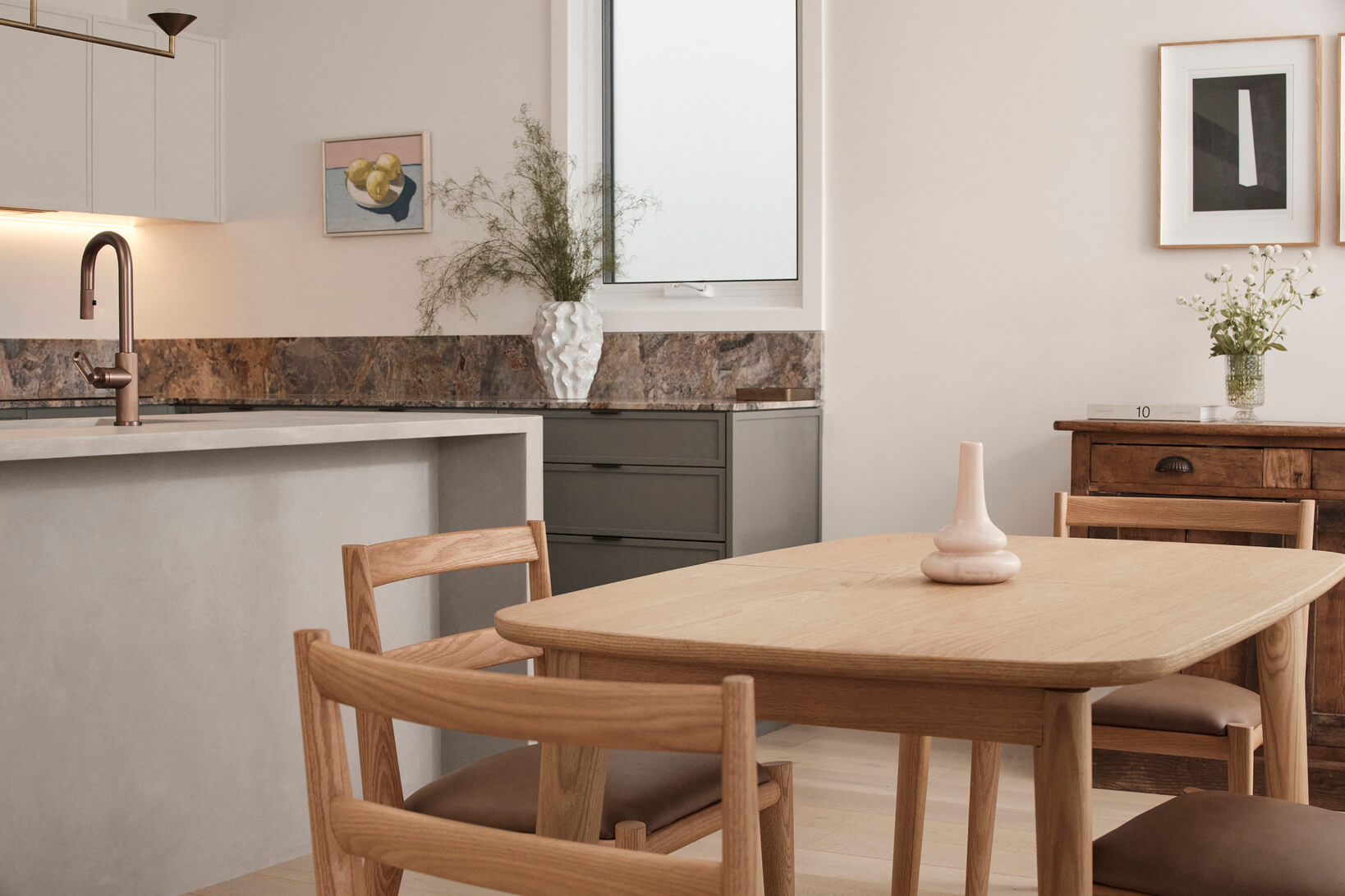 Light timber dining setting in an open plan kitchen, contemporary and minimalistic, styled with ceramic vases and tall plants.